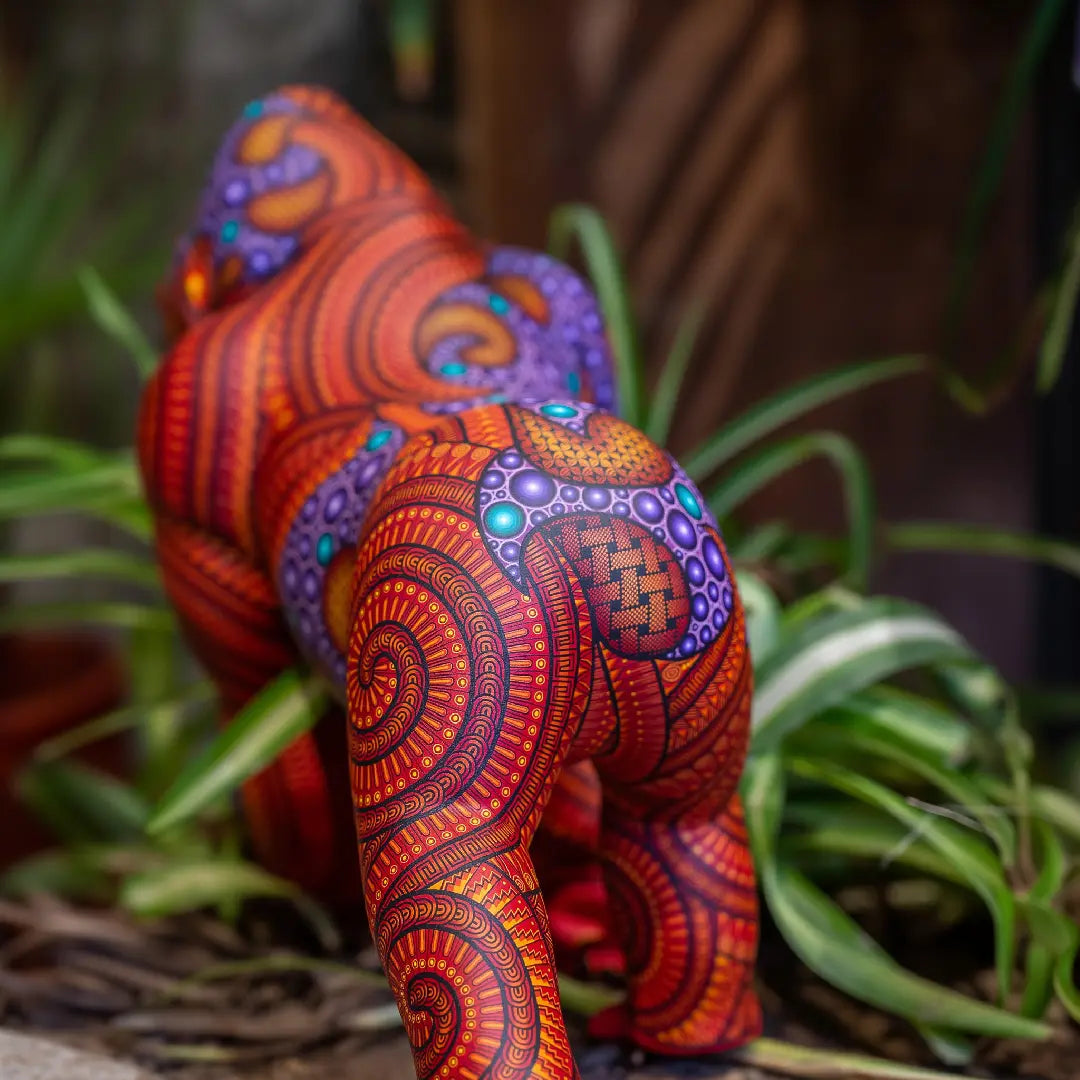 Hand-painted gorilla alebrije with vibrant patterns and intricate Mexican folk art details, displayed with tropical plants in the background