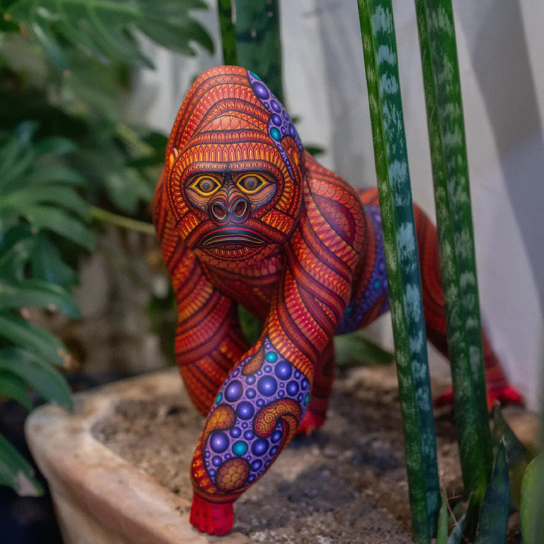 Hand-painted gorilla alebrije with vibrant patterns and intricate Mexican folk art details, displayed with tropical plants in the background