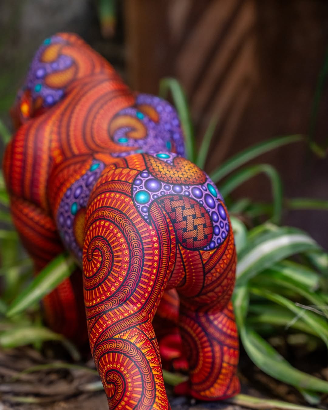 Hand-painted gorilla alebrije with vibrant patterns and intricate Mexican folk art details, displayed with tropical plants in the background